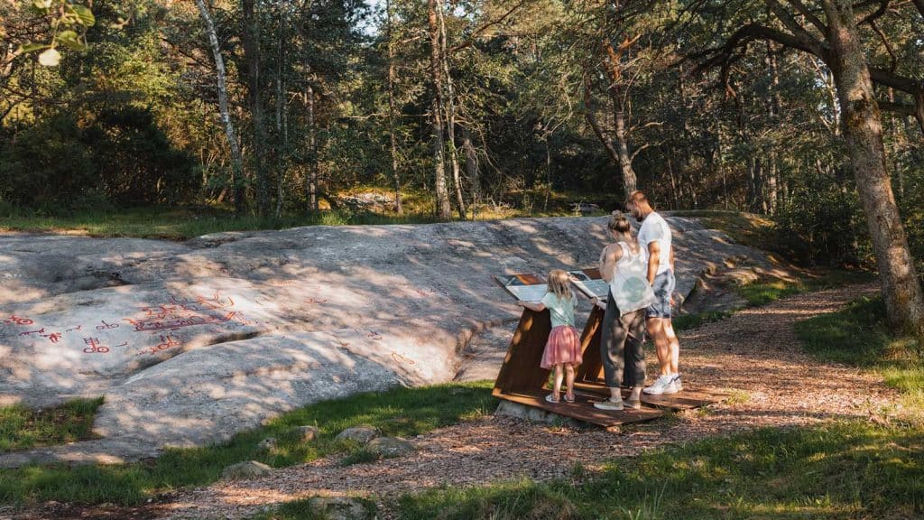 Familie ser på helleristninger på Begbyfeltet i Fredrikstad, figurer fra bronsealderen hugget inn i fjell.