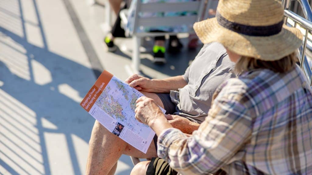 To personer ser på kart over Hvaler og øyhoppingsruta mens de sitter på dekk med solhatt.