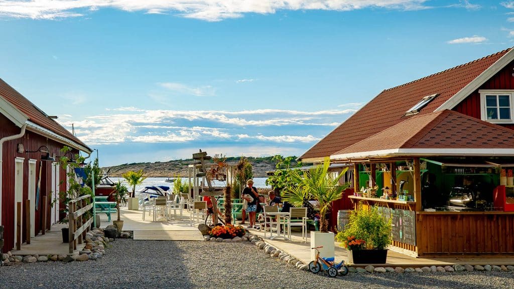 Marina med røde sjøhus, palmer og uteservering mot sjøen.