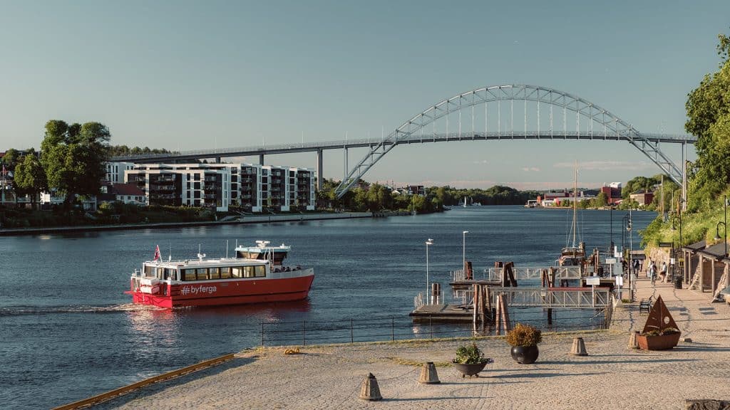ød byferge kjører på elva i Fredrikstad med bro og moderne bygninger i bakgrunnen