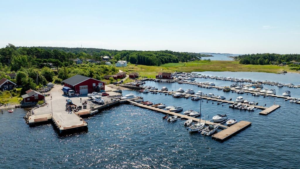 Utsikt over Nedgården havn på Søndre Sandøy, med båthavn, røde naust, fergeleie og frodig landskap i bakgrunnen.