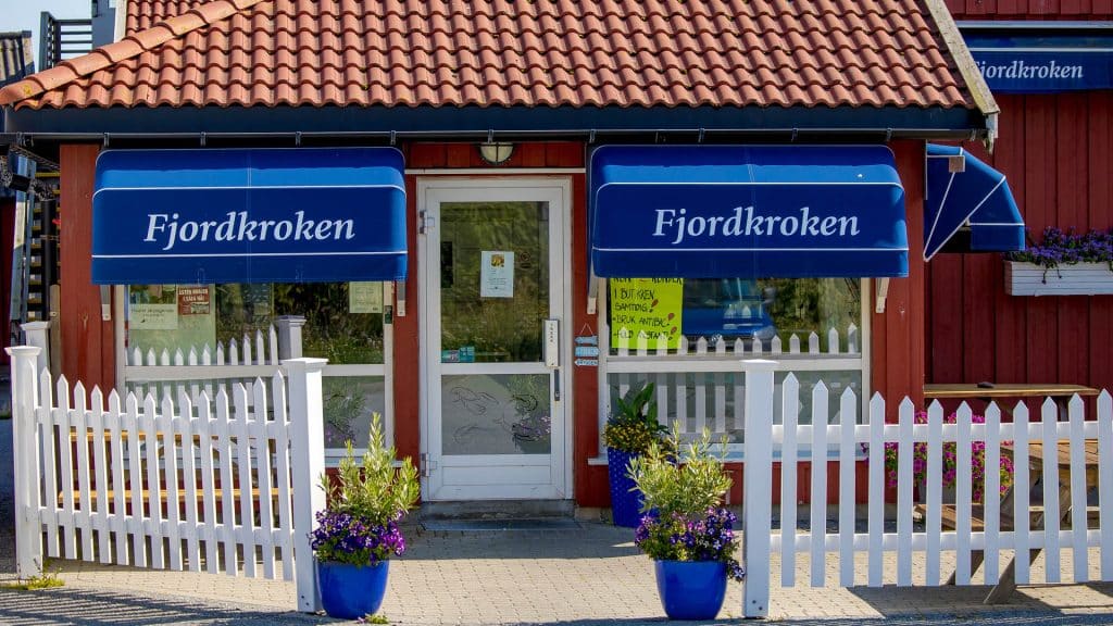 Inngang til butikk med blå markiser og hvitt stakittgjerde ved sjøen.