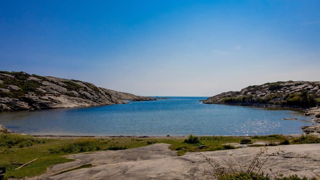 Guttormsvauen med bukt, strand og svaberg under blå himmel.