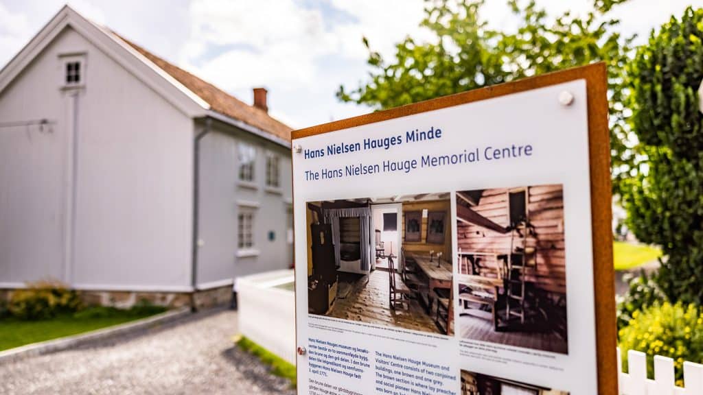 Skilt ved Hans Nielsen Hauges Minde med bilde av barndomshjemmet og besøkssenter.