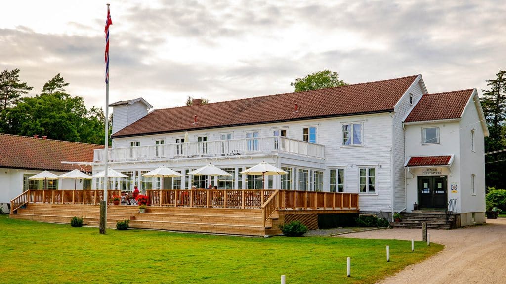 Fasade av Hvaler Gjestgiveri med inngangsparti, flaggstang og terrasse med parasoller