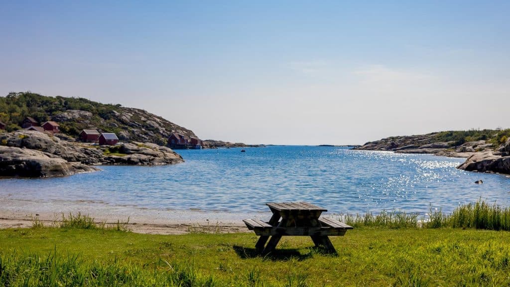 Kuvauen med piknikbenk i forgrunnen og røde sjøboder langs bukta.