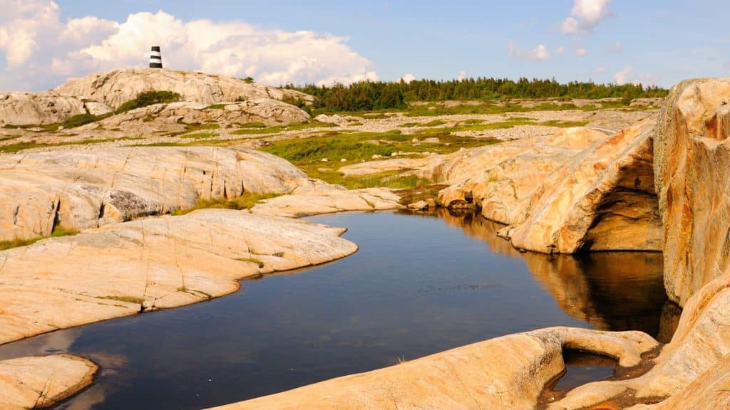 Utsikt mot Linnekleppen sjømerke og kystlandskapet på Herføl, med jettegryta Kjerka i forgrunnen omgitt av svaberg.