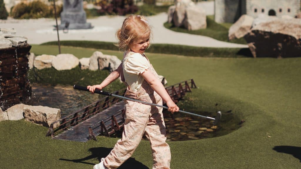 Lite barn spiller minigolf på grønn bane med små broer og vann