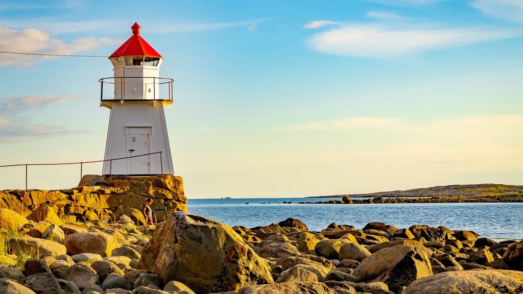 Hvit fyrlykt med rød topp ved Pikesten på Brattestø, omgitt av svaberg og hav i gyllent ettermiddagslys.