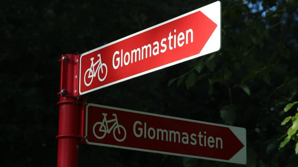 Røde sykkelskilt som viser retningen til Glommastien, omgitt av mørk skog.