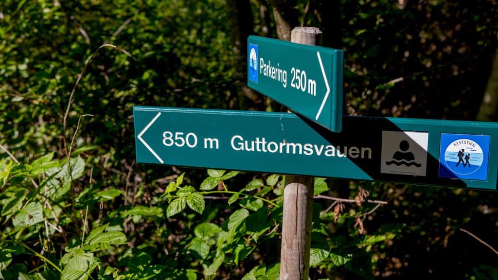 Skilt som viser vei til Guttormsvauen og parkering, omgitt av grønn vegetasjon.