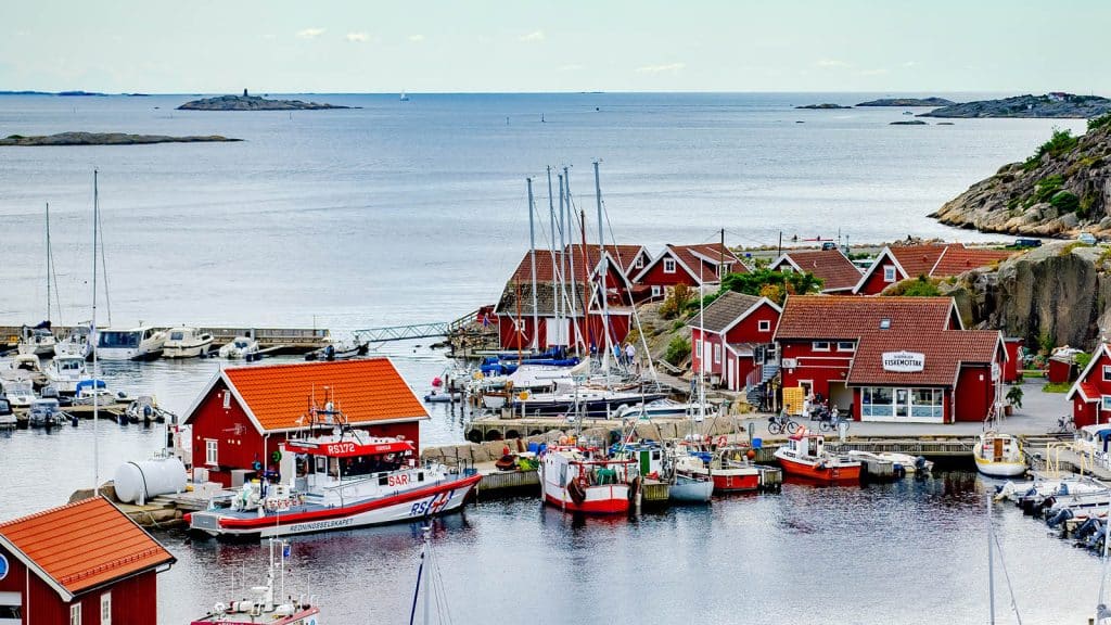 Oversikt over småbåthavn og røde sjøhus ved kysten.