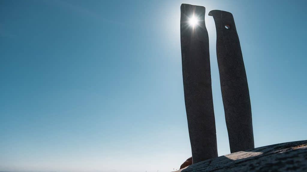 To høye granittsøyler står oppreist blant svaberg på Rødshue, med hav og himmel i bakgrunnen.