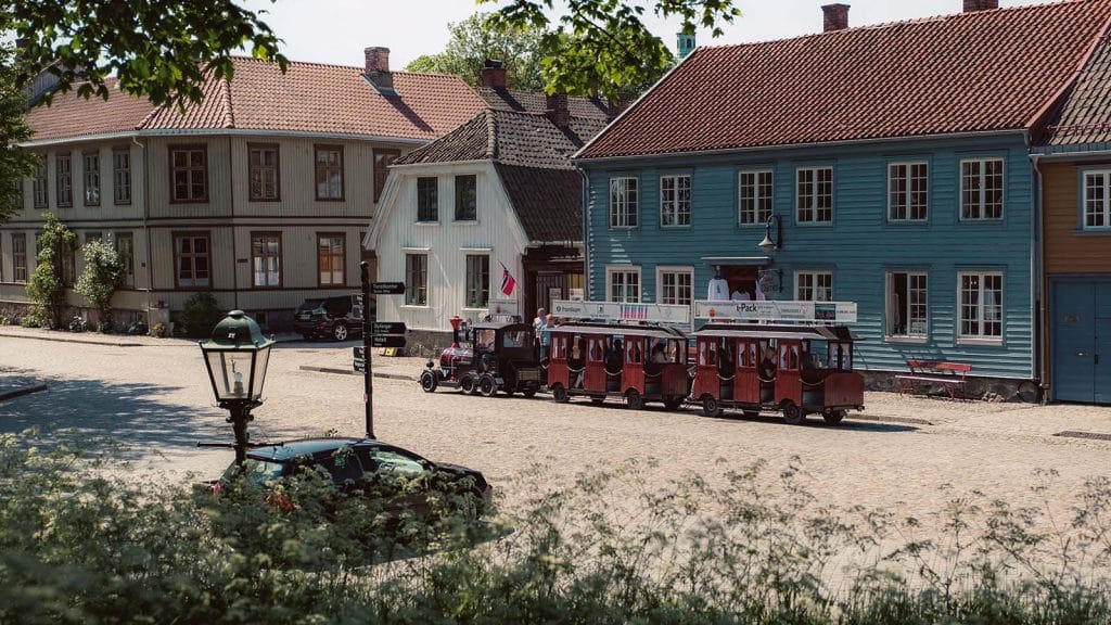 Turisttog kjører gjennom Gamlebyen i Fredrikstad med fargerike trehus rundt