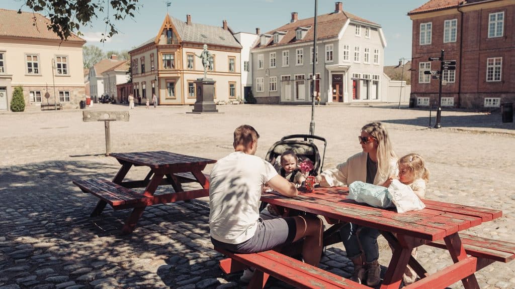 Familie med små barn sitter ved bord på torget i Gamlebyen.