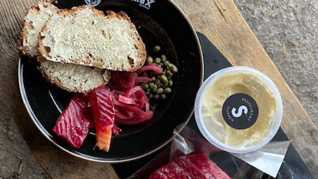 Tallerken med gravlaks, brød, løk og kapers på en benk.