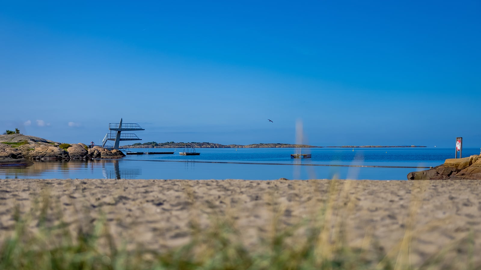 Badeplass med stupetårn og badebrygger ved Foten friluftsområde på Hvaler, med blå himmel og rolig sjø.