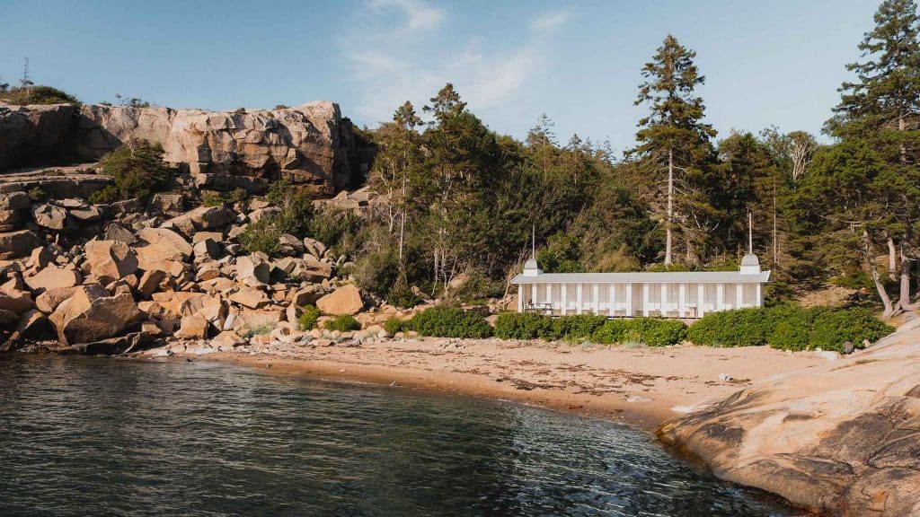 Hvitt badehus ved Trouville-stranden på Hankø, omgitt av svaberg og skog.