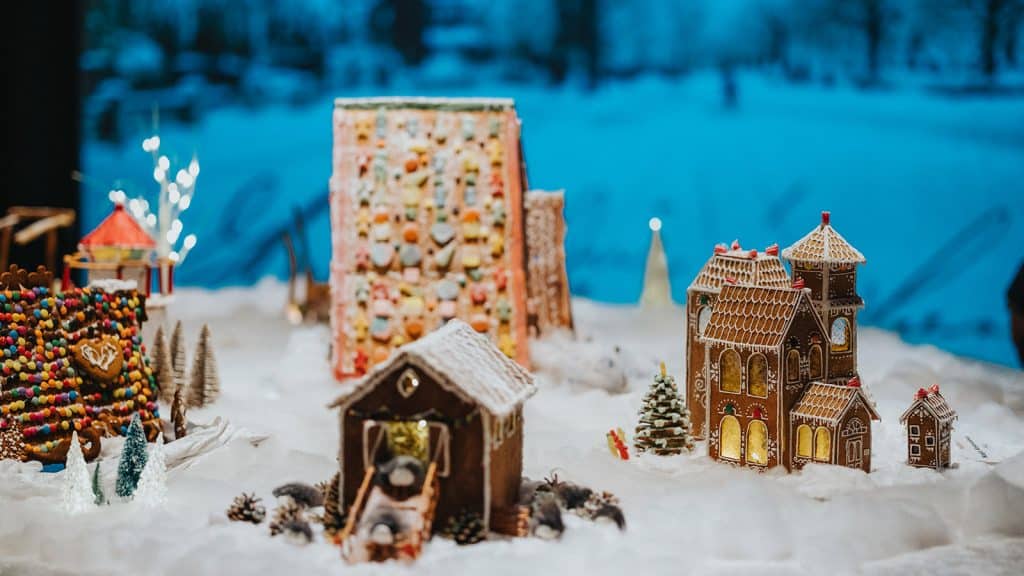 Detaljert pepperkakeby med hus, trær og figurer, utstilt i vinterlig landskap med blå bakgrunn.