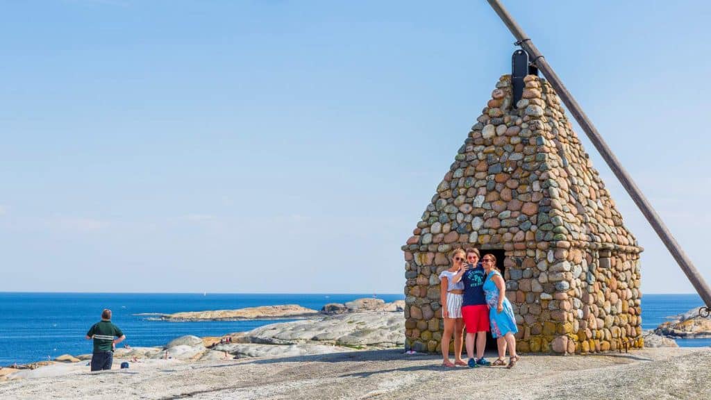 Familie poserer foran varde med vippefyr ved Verdens Ende i Vestfold, med utsikt over skjærgård og hav.