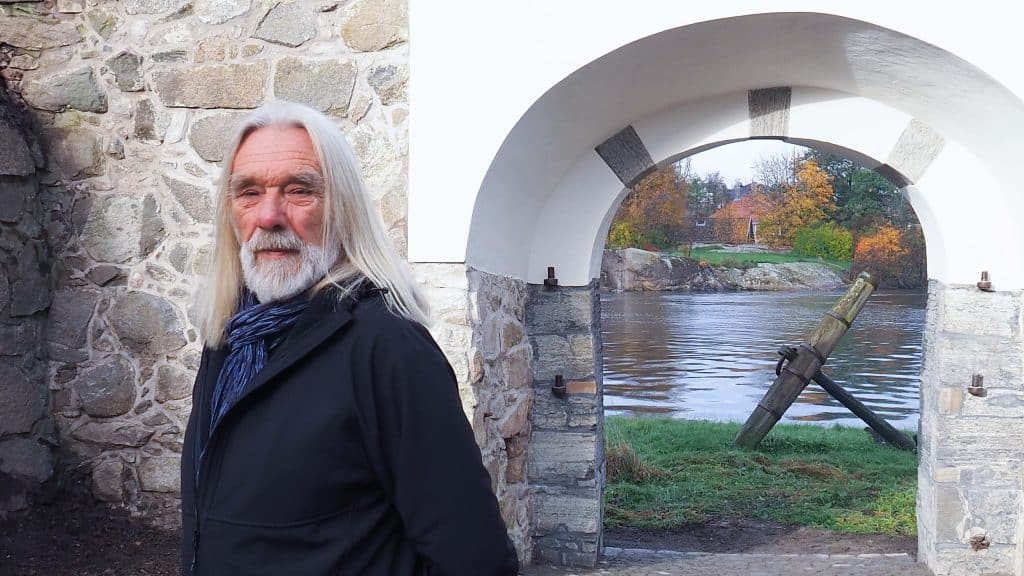 Guide Arild står ved en steinport i Gamlebyen med elven og høsttrær i bakgrunnen.