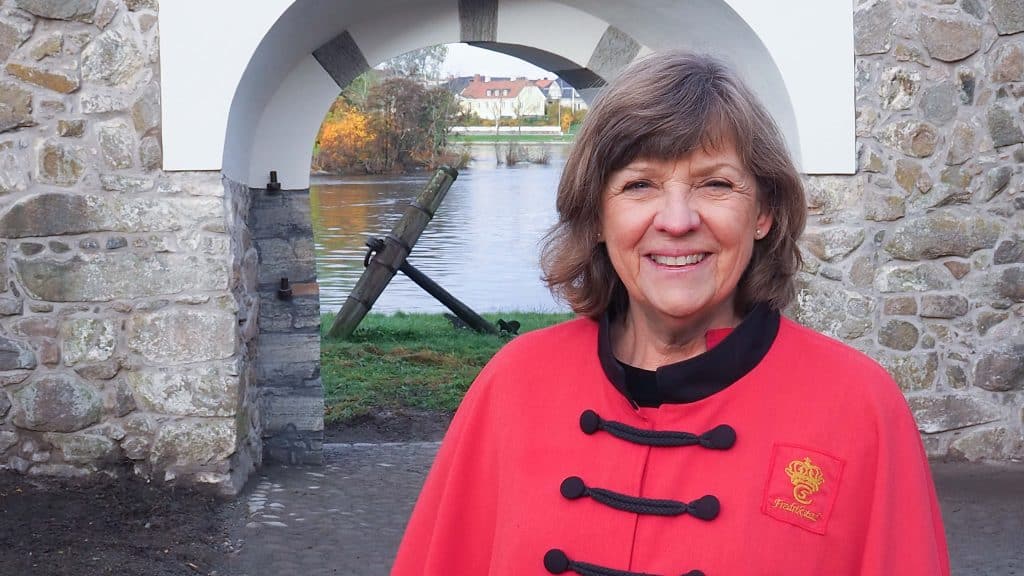 Guide Christine smiler foran festningsmur og port i Gamlebyen i Fredrikstad.