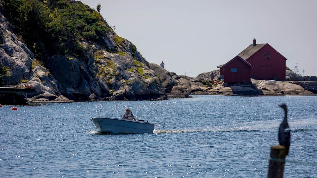 Person i liten motorbåt på sjøen ved Utgårdskilen, omgitt av svaberg og røde sjøboder.