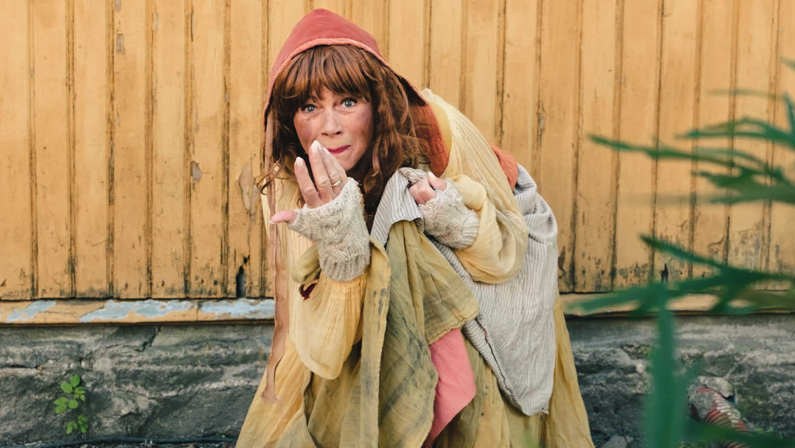Karen Øltapper i historisk kostyme foran en gul trevegg i Gamlebyen.