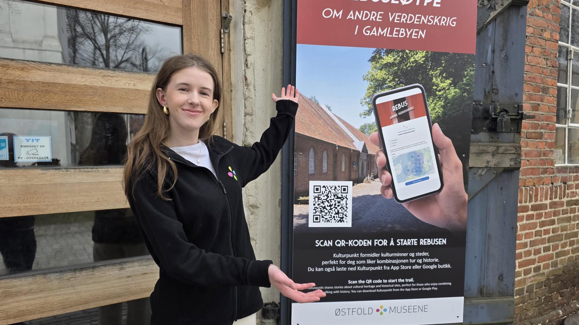 Ung kvinne står ved en plakat for en digital rebusløype om andre verdenskrig i Gamlebyen.