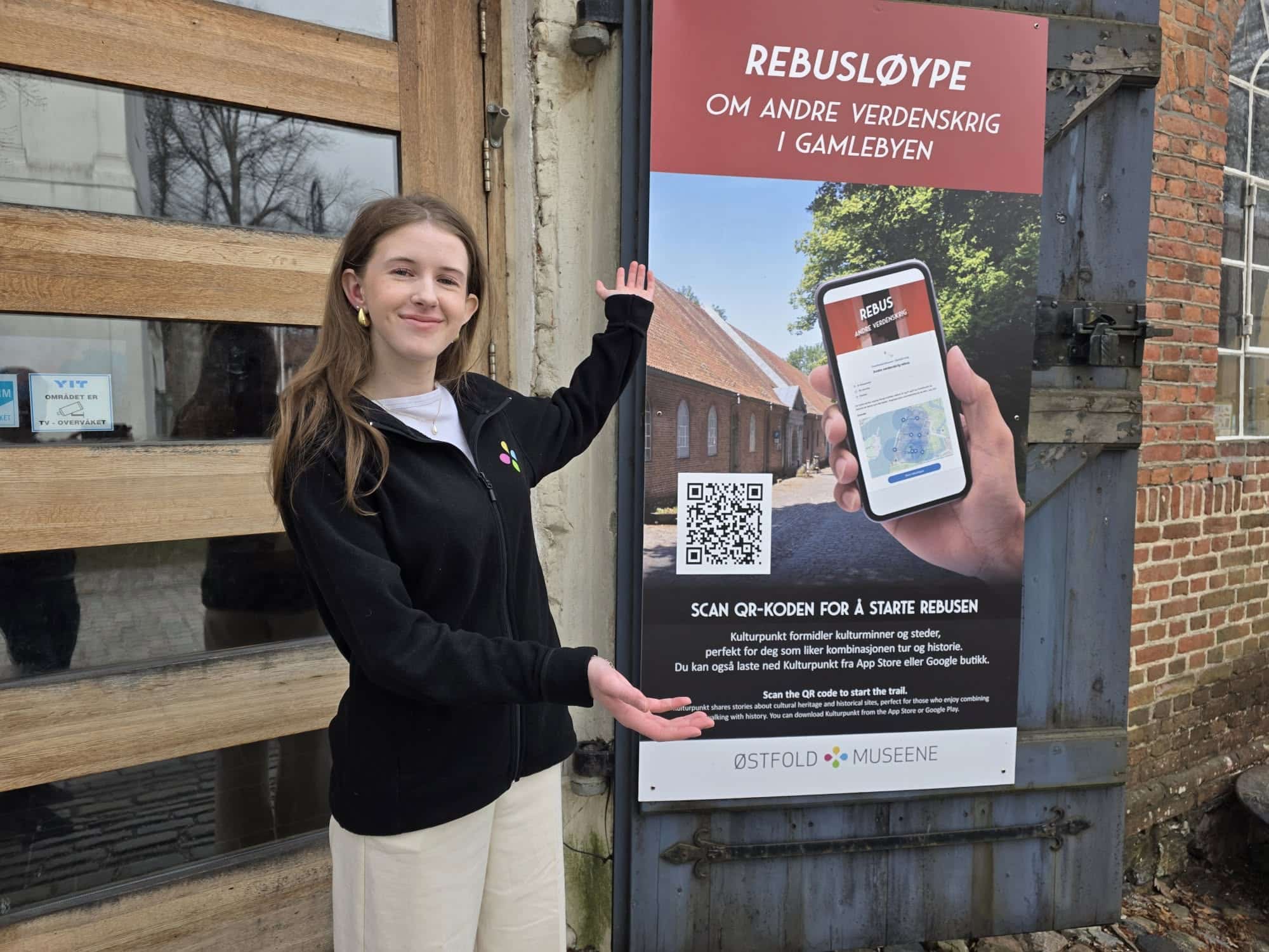 Ung kvinne står ved en plakat for en digital rebusløype om andre verdenskrig i Gamlebyen.